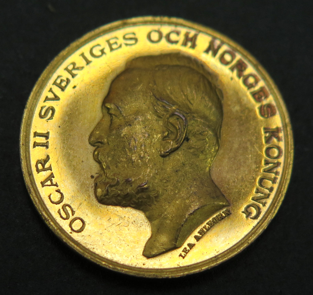 Minnesmedalj, förgylld brons, Industriutställningen i Stockholm 1897, dekor av konung Oskars II porträtt, gravör Lea Ahlborn, dia 25 mm